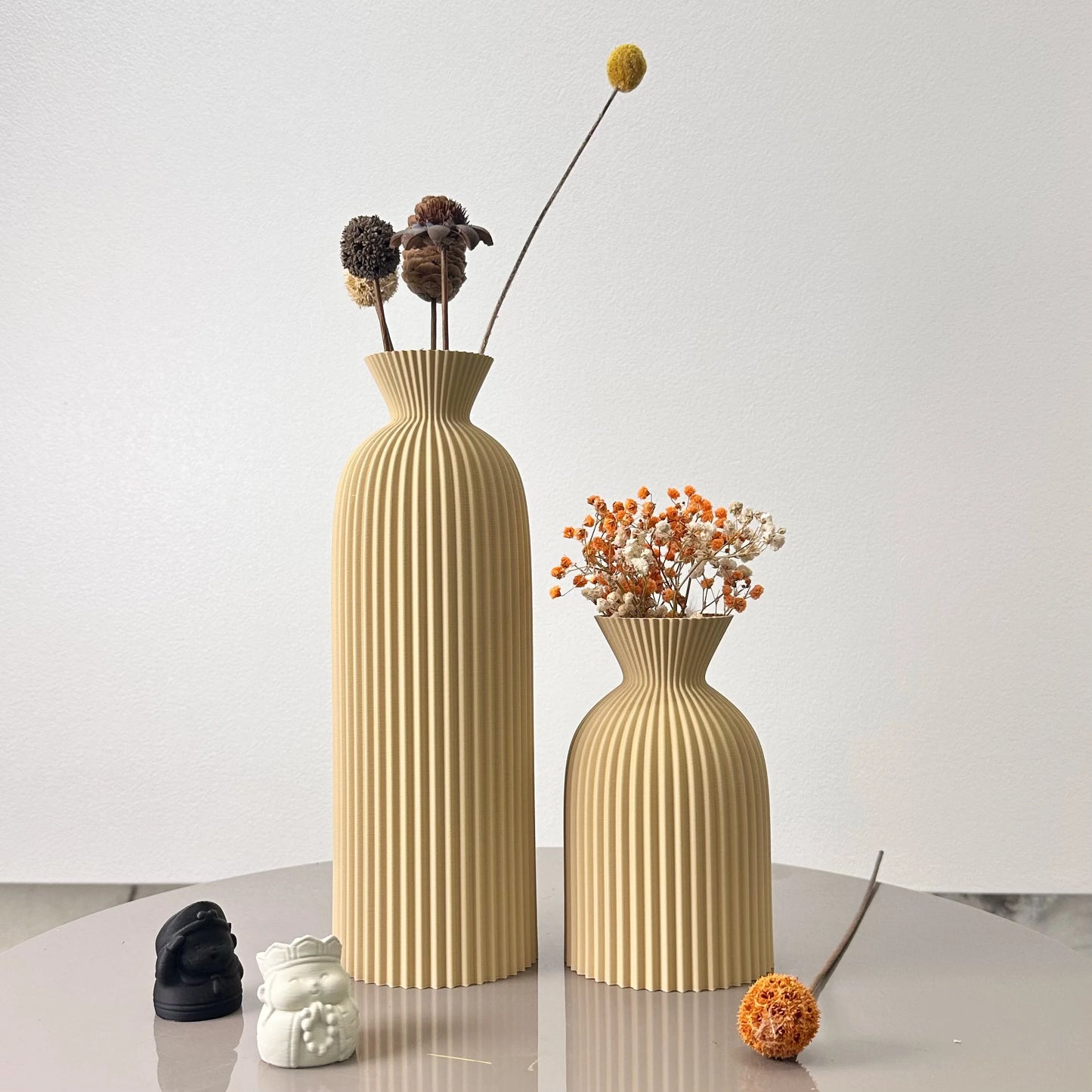 Two beige vases with dried flowers on a light surface and white background