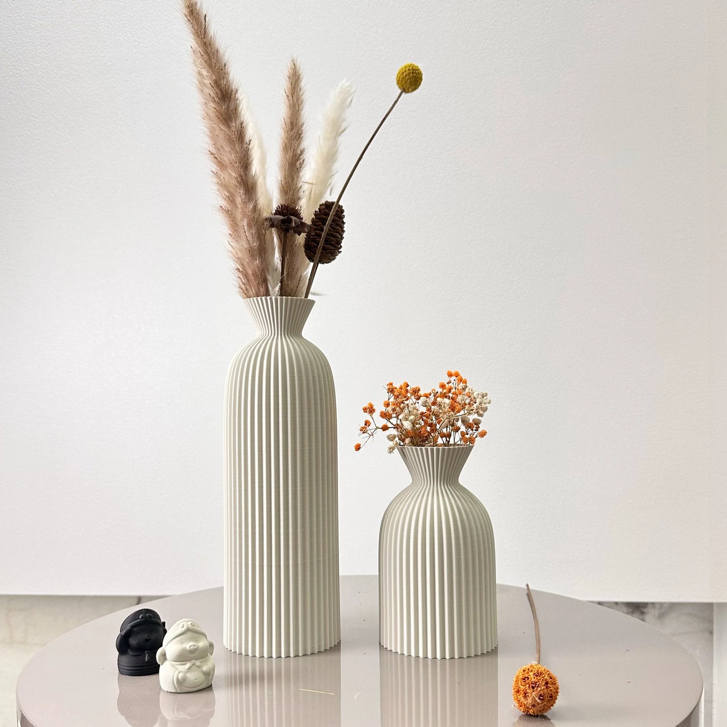 Two decorative vases with dried plants on a white surface