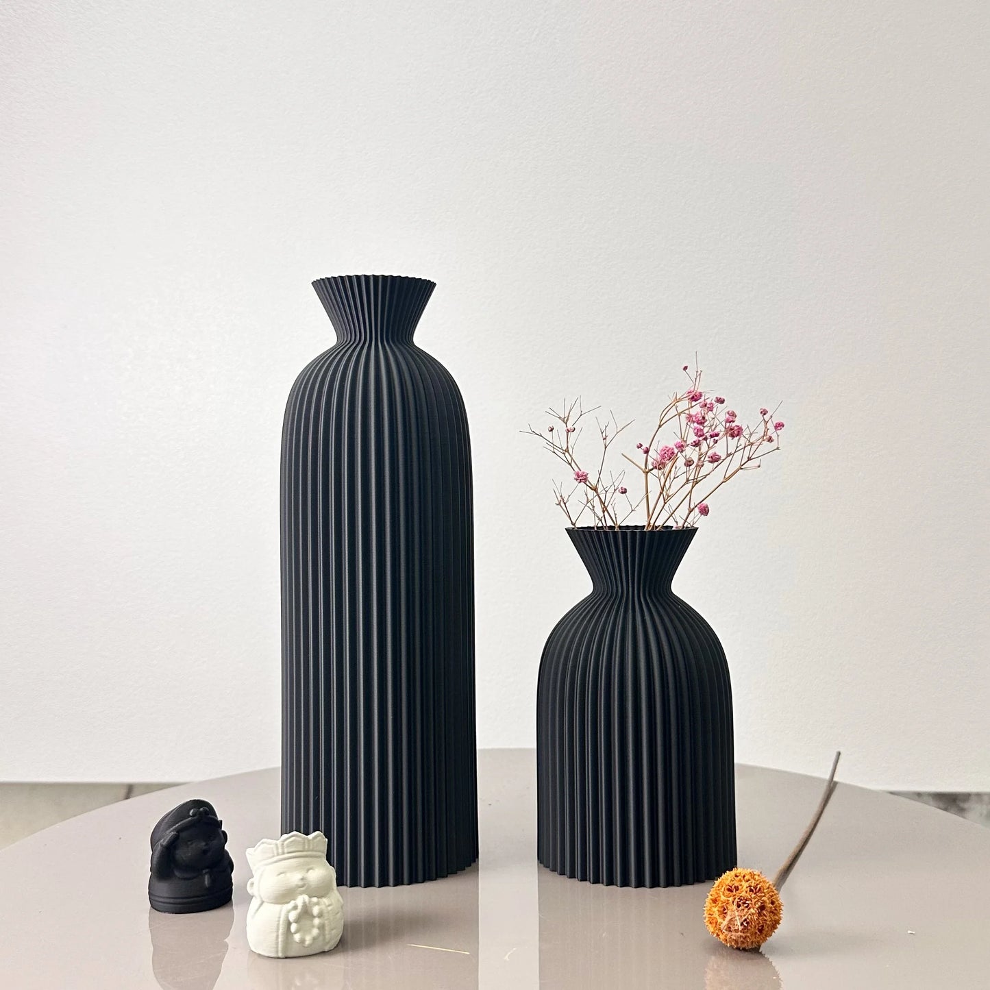 Two black vases on a white surface with a plain background