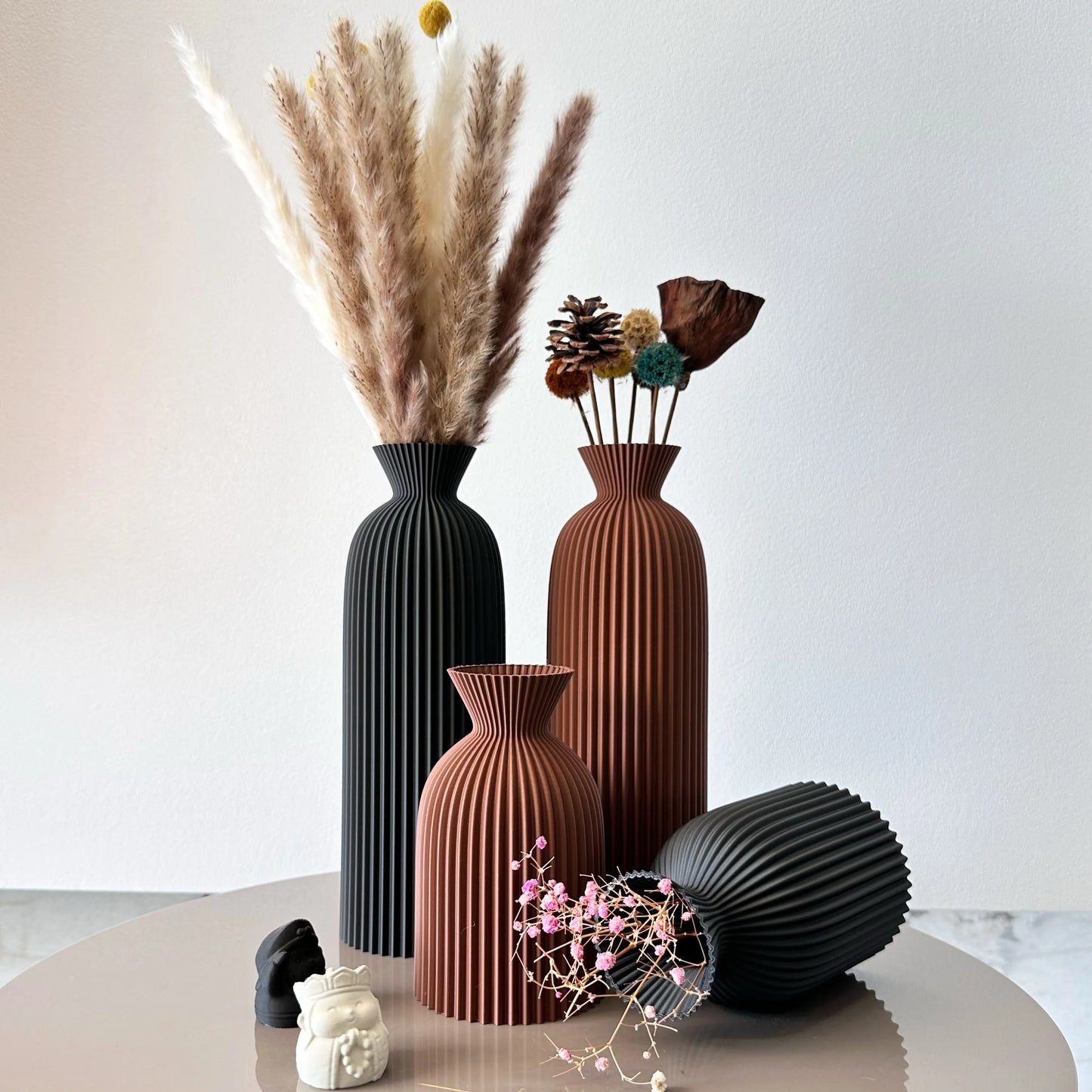 Set of decorative vases with floral and pinecone arrangements on a white surface.