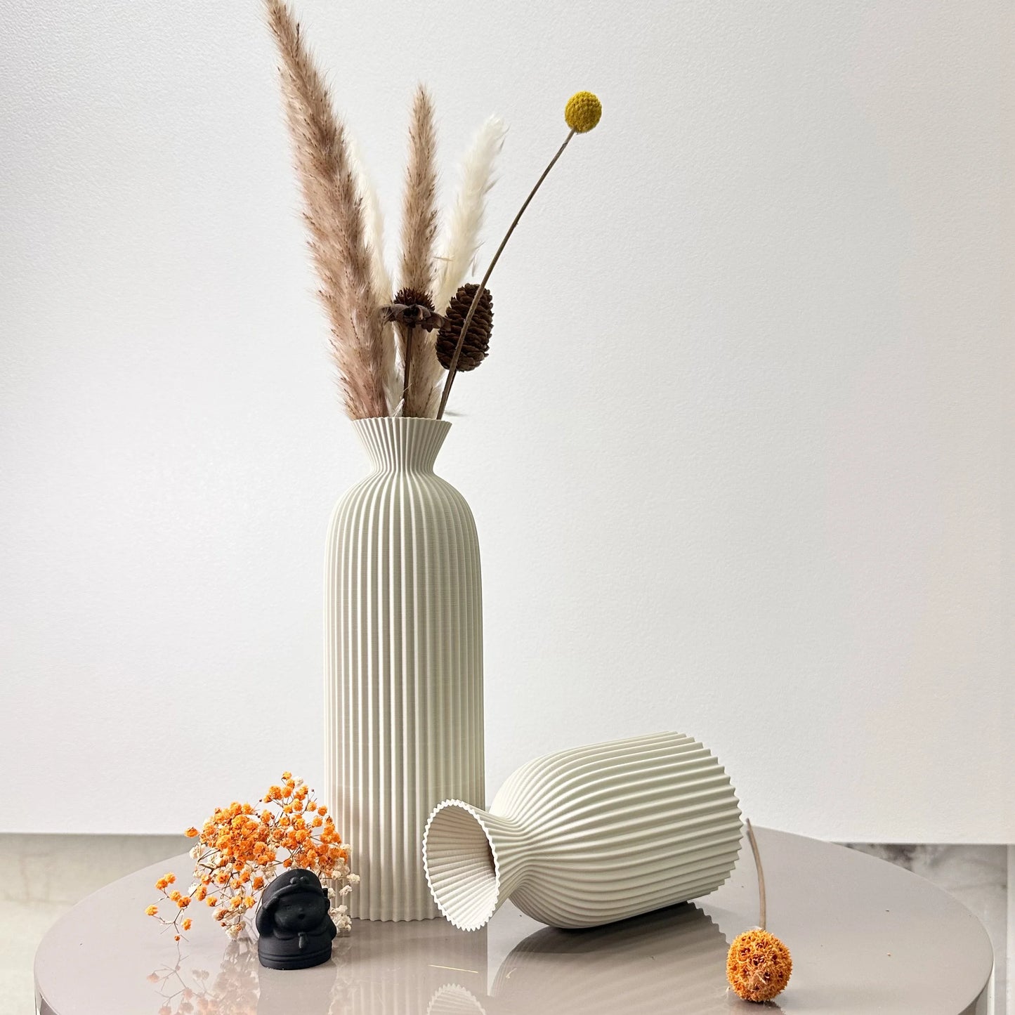 Decorative vases with dried plants on a light surface