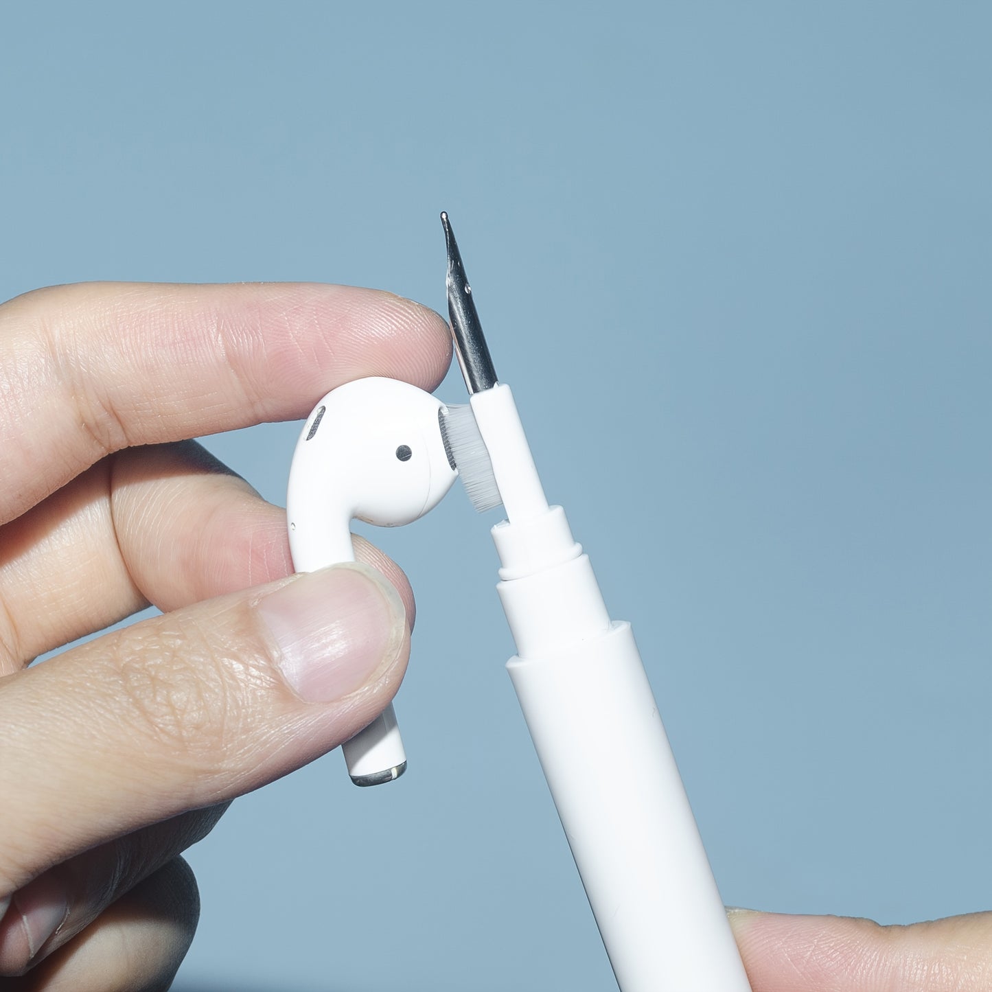 White earbud being adjusted with a white pen against a light blue background
