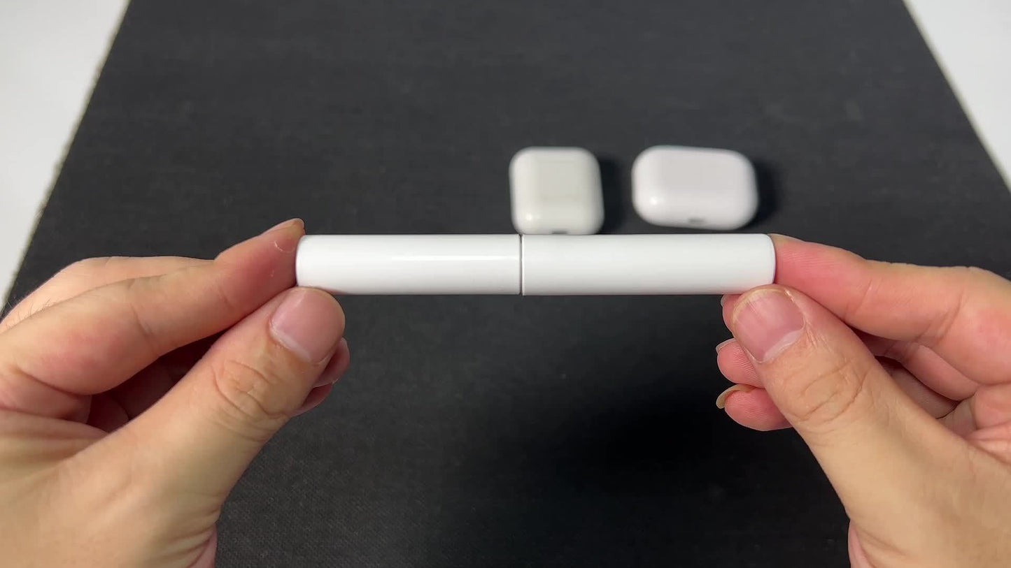 Two hands holding a white cylindrical object with two small square objects on a dark surface.
