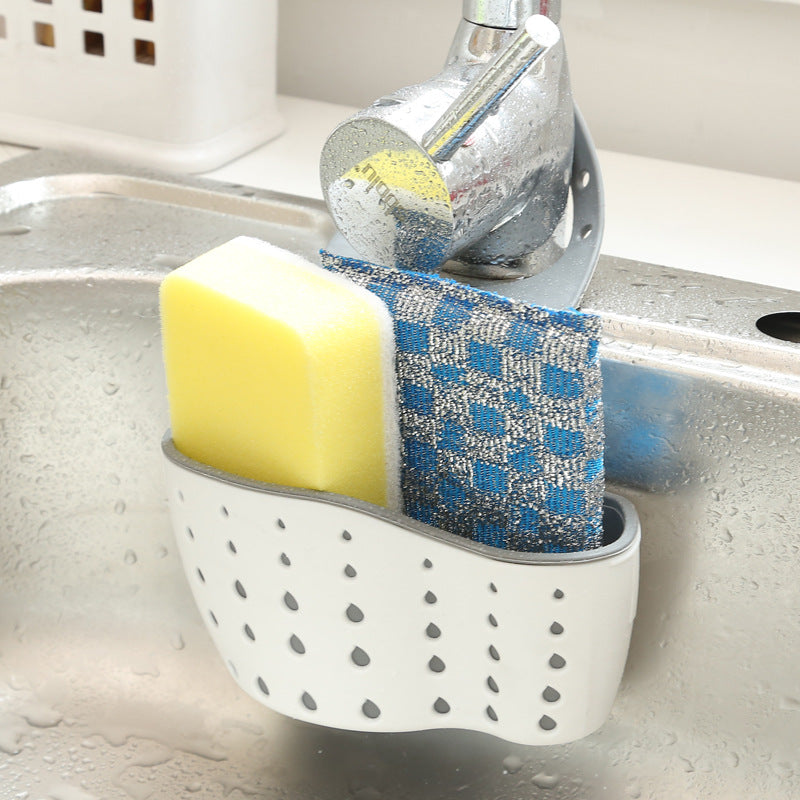 Kitchen sink caddy holding a sponge and scrubber next to a faucet.