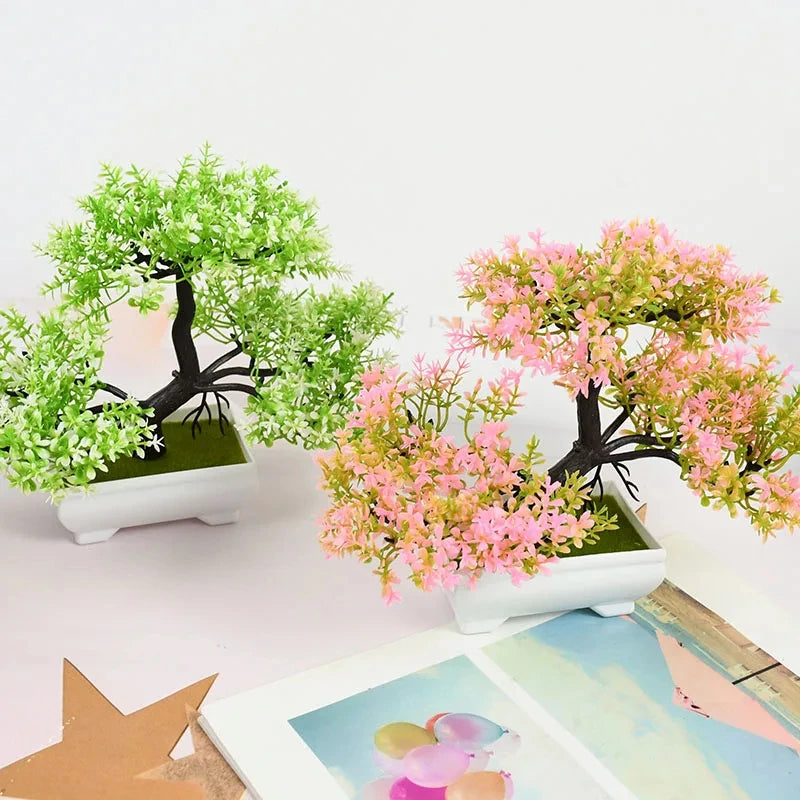Two small artificial bonsai trees, one green and one pink, on a white surface.