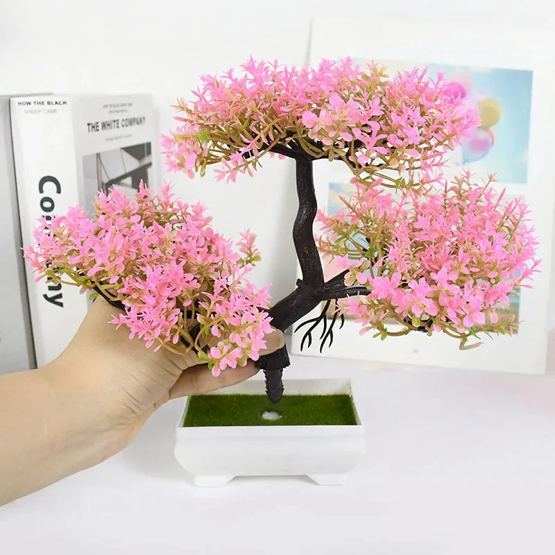 Small potted bonsai tree with pink flowers held by a hand on a white surface.
