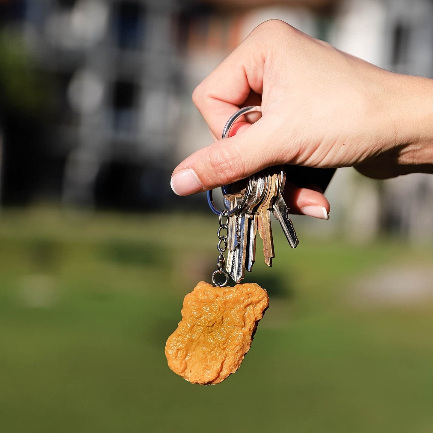 Hand holding keys with a dog tag shaped like a paw print against a blurred outdoor background