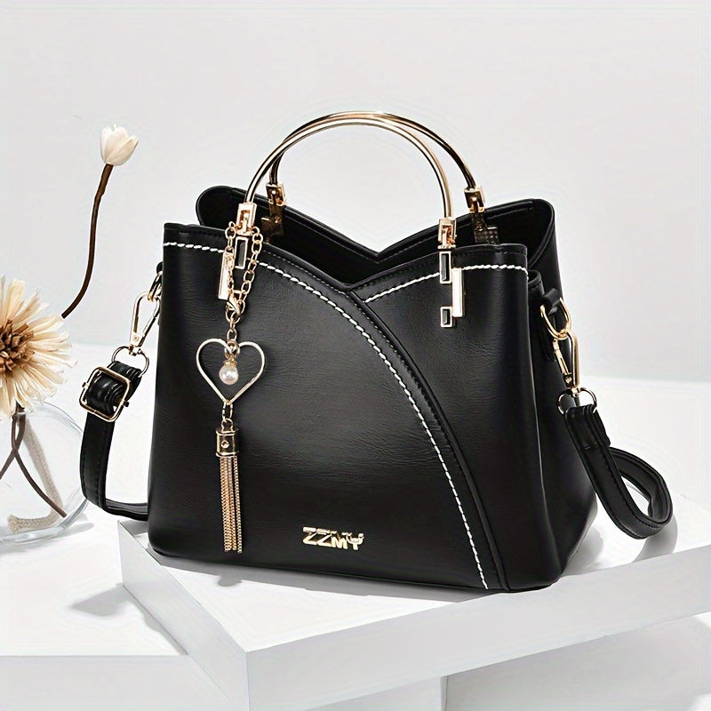 Black handbag with gold accents and a heart-shaped keychain on a white surface.