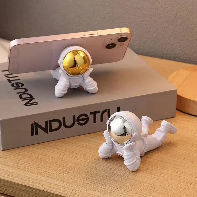 Phone holder shaped like an astronaut with gold and silver reflective heads on a wooden surface.