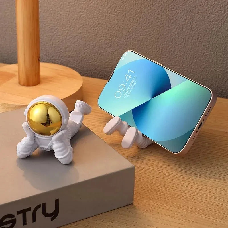 Phone holder shaped like an astronaut next to a smartphone on a wooden surface