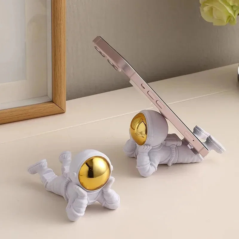 Two white astronaut phone holders with gold accents on a light surface.