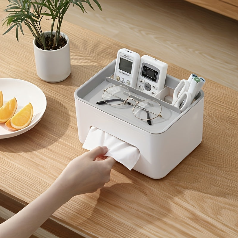 White paper towel holder on a wooden table with a hand pulling a towel, next to a plant and plate of fruit.