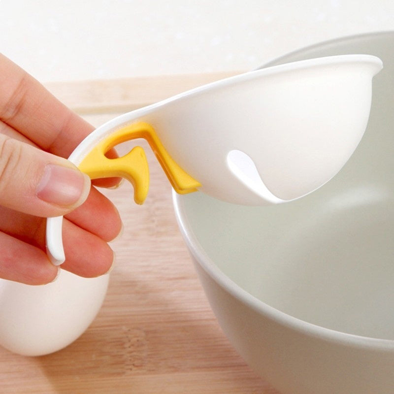 Hand holding a white egg separator with a yellow handle over a white bowl on a wooden surface.