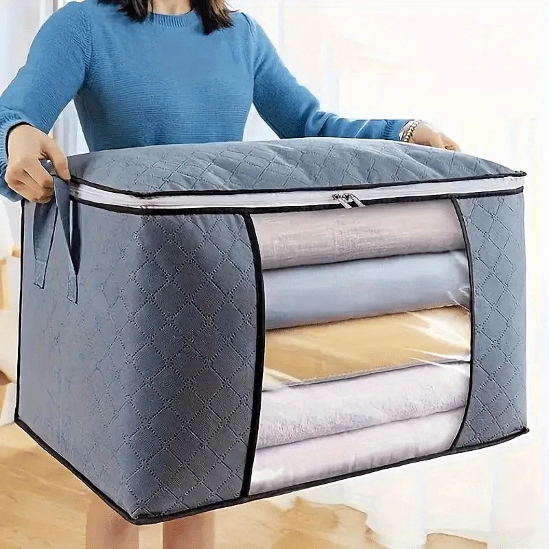 Person holding a large gray storage bag with quilted texture, containing folded clothes.