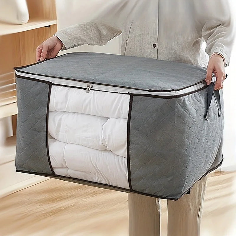 Person holding a gray storage bag with white bedding inside on a wooden floor.