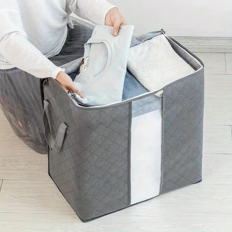 Person organizing clothes into a large gray storage bag on a wooden floor.