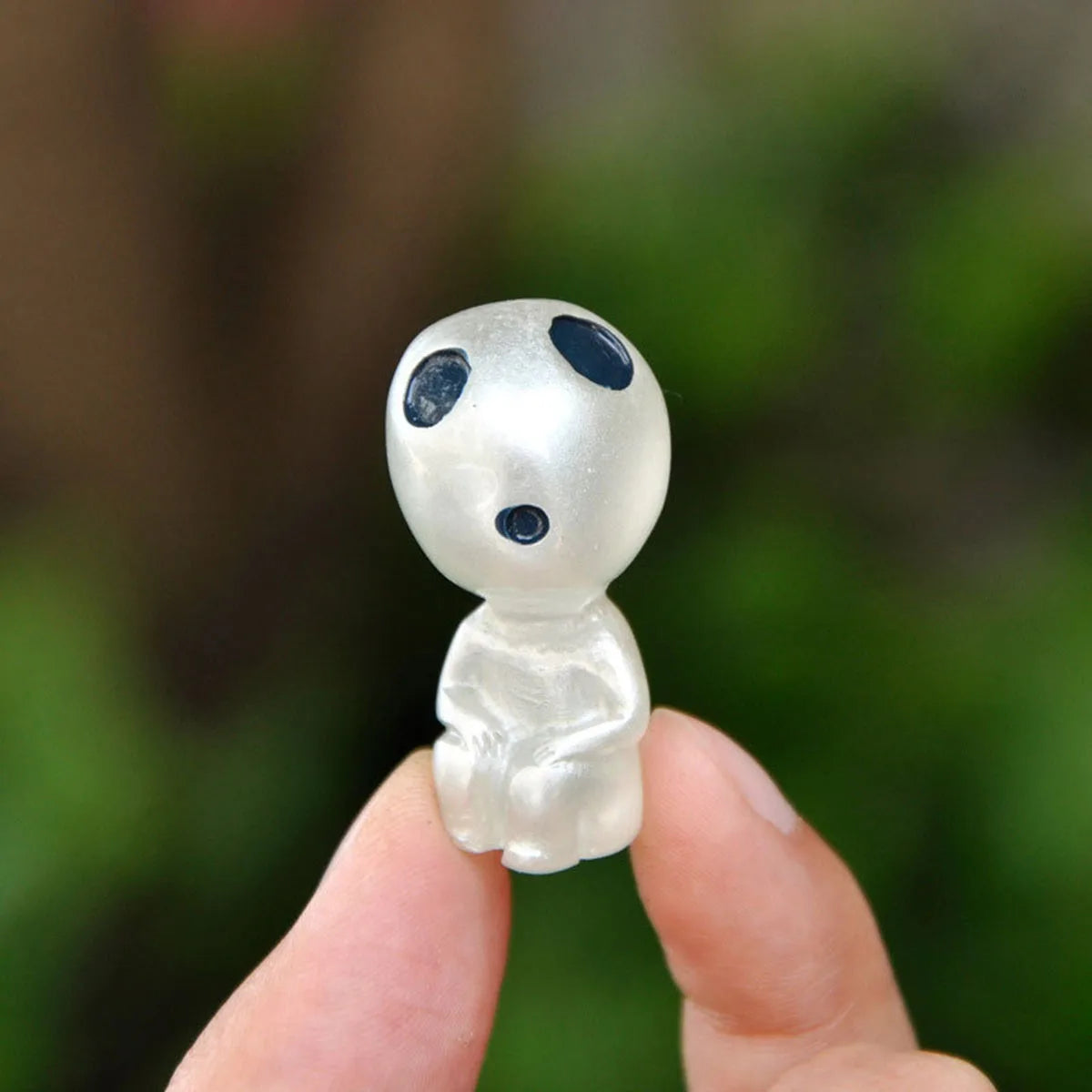 Small alien figurine held in a hand with a blurred green background