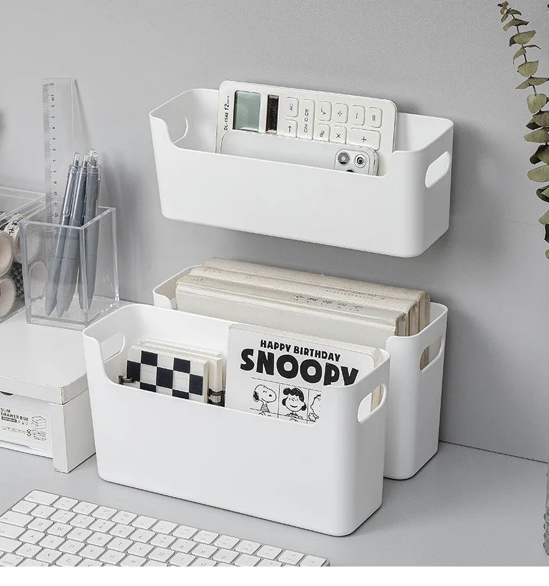 White storage baskets on a desk with books and stationery items.