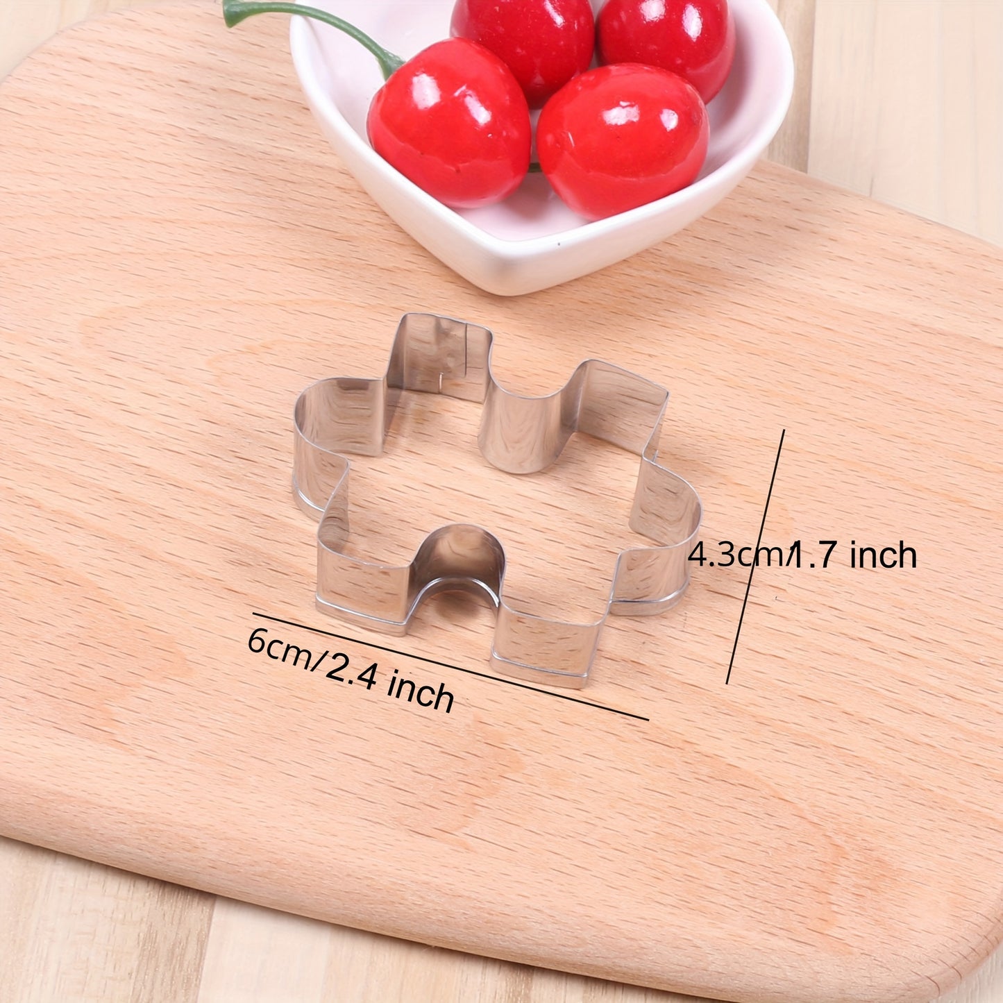 Metal cookie cutters shaped like cookies on a wooden board with a bowl of cherries in the background.