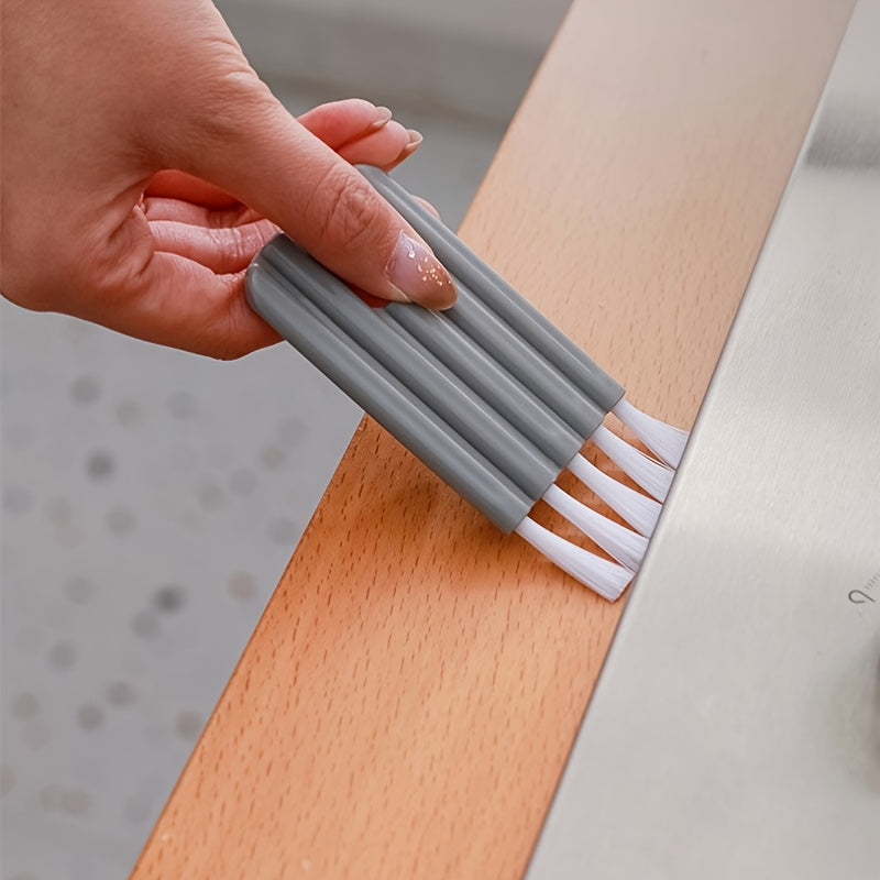 Person using a gray bristle brush with white bristles on a wooden surface.