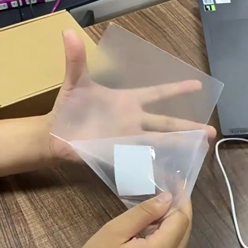Hand holding a clear plastic sheet with a white square on a wooden surface.