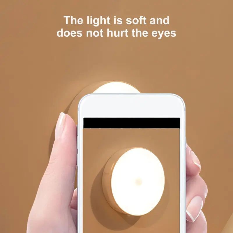 Hand holding a smartphone with a circular light on a brown background, text 'The light is soft and does not hurt the eyes'.
