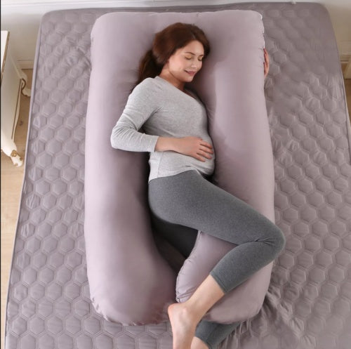 Woman lying on a hexagonal patterned mattress with a large gray body pillow.