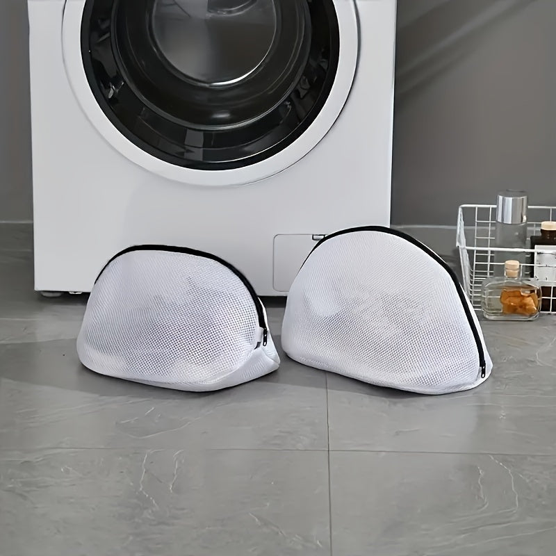 Two white mesh laundry bags with black zippers on a gray floor in front of a washing machine.
