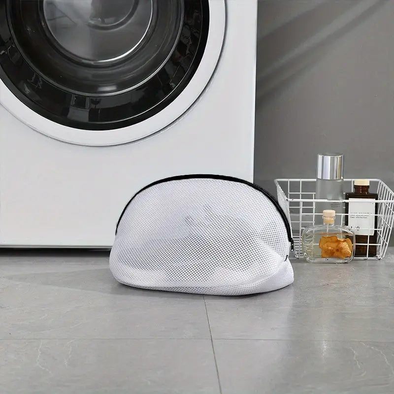White mesh laundry bag on the floor in front of a washing machine.