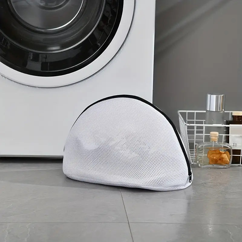 White mesh laundry bag on a gray floor in front of a washing machine.
