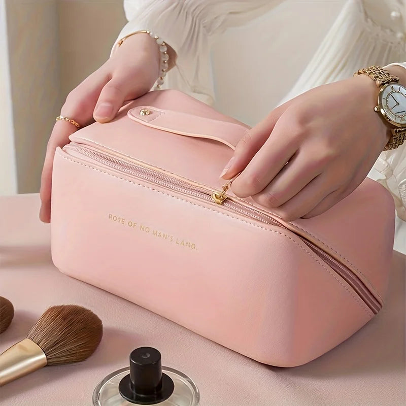 Pink cosmetic bag with gold accents held by a person, surrounded by makeup items on a light surface.