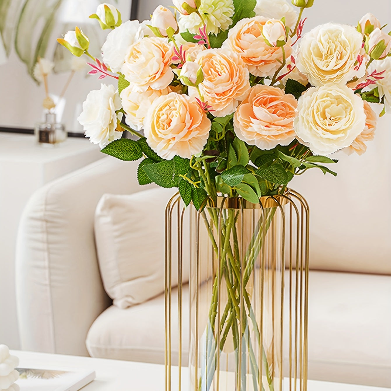 Bouquet of peach and white roses in a gold vase on a table with a blurred background