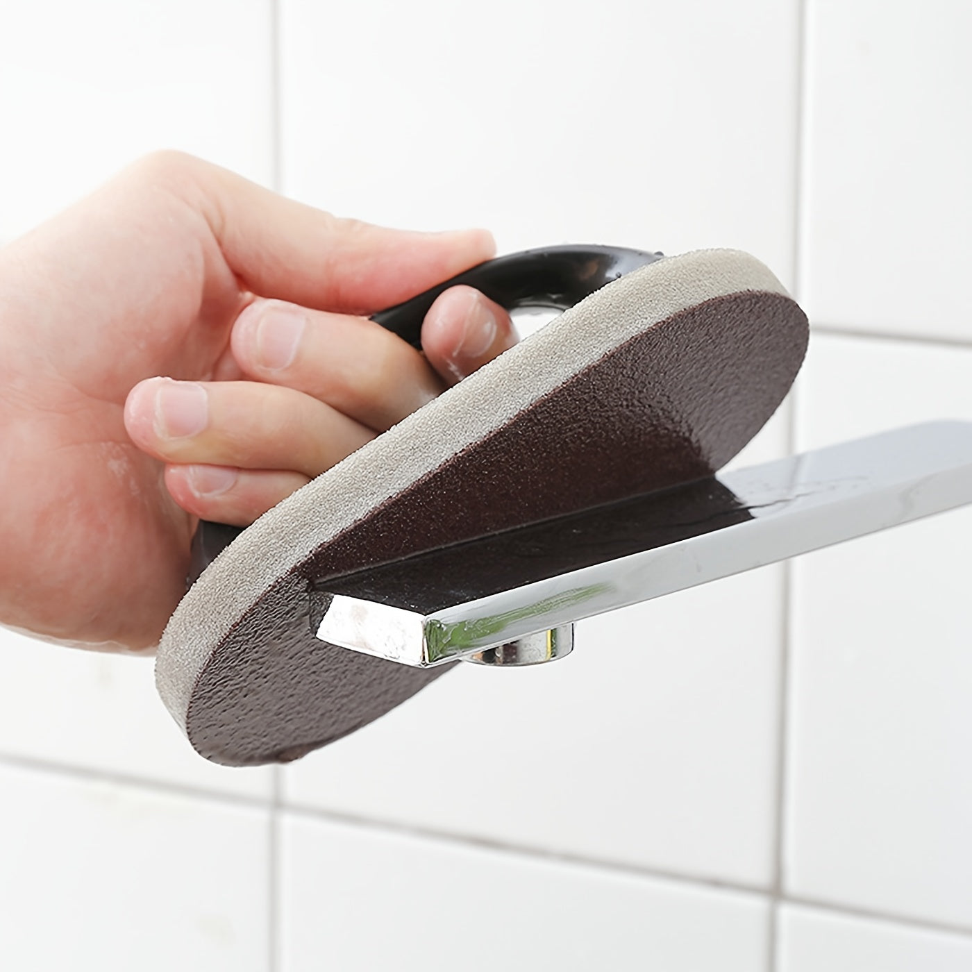 Hand holding a shower head with a sanding pad against a tiled wall background