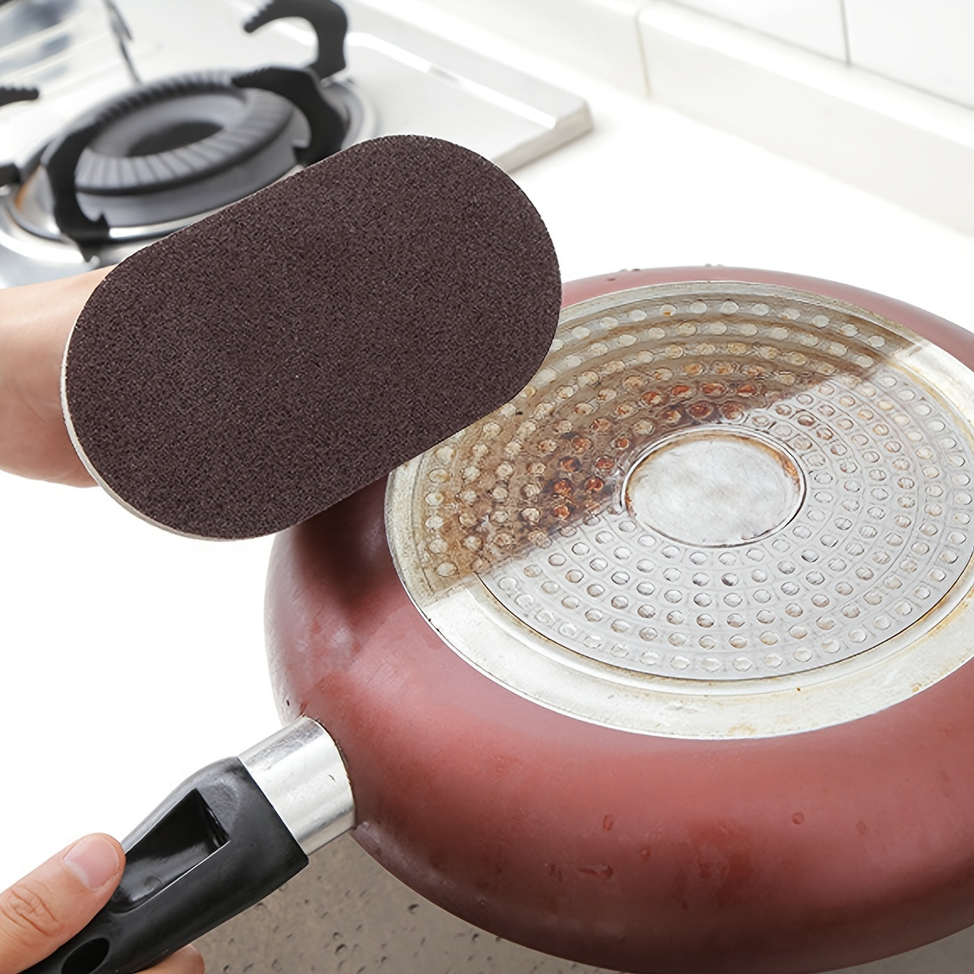 Person using a scrubber to clean a rusty frying pan on a stove.