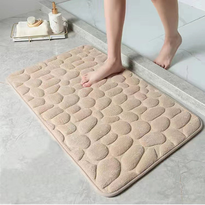 Beige textured bath mat on a bathroom floor with a person stepping onto it.