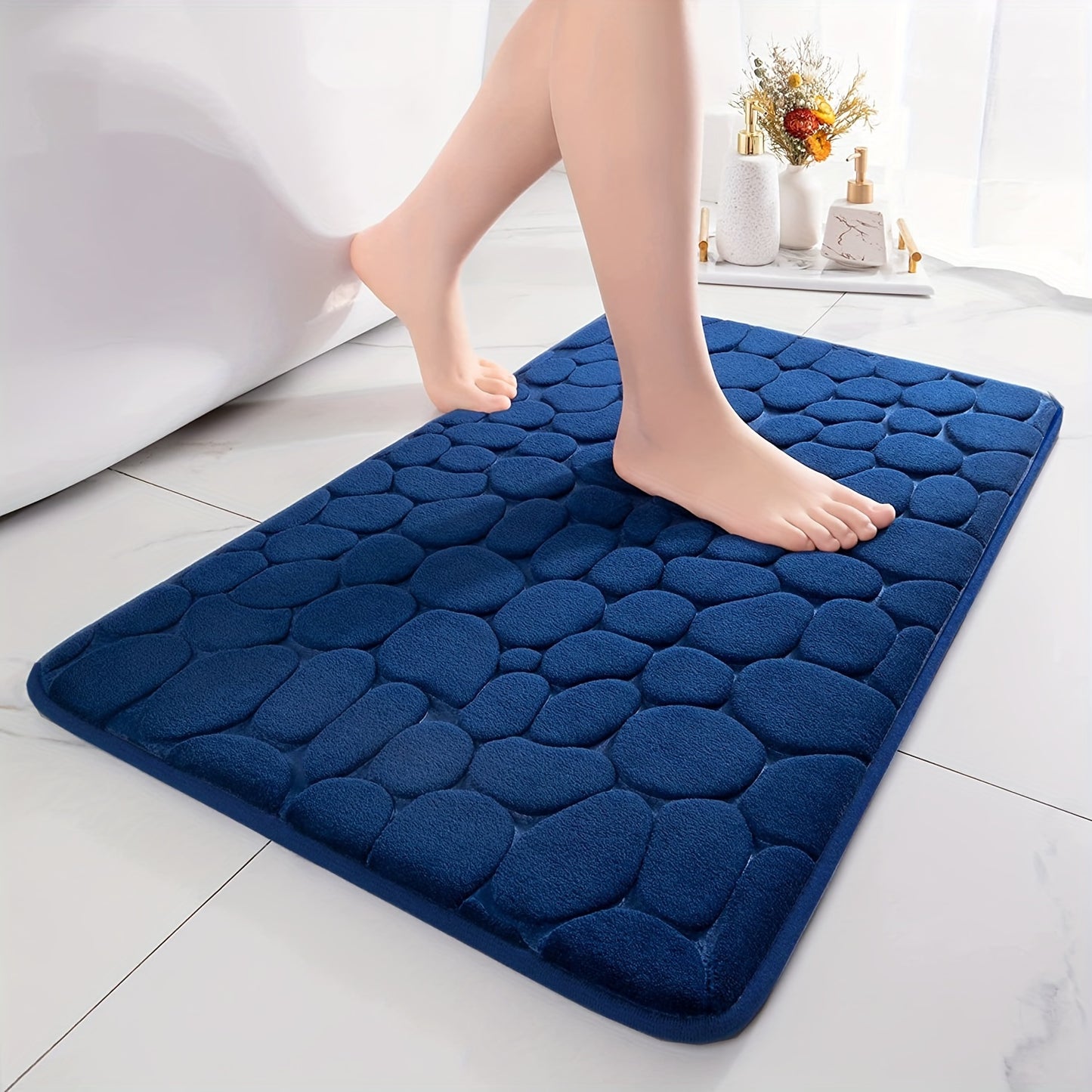 Blue textured bath mat with feet stepping onto it in a bathroom setting.