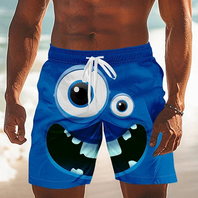 A man wearing bright blue swim trunks with a large cartoon monster face graphic, shown from the chest down on a beach background.