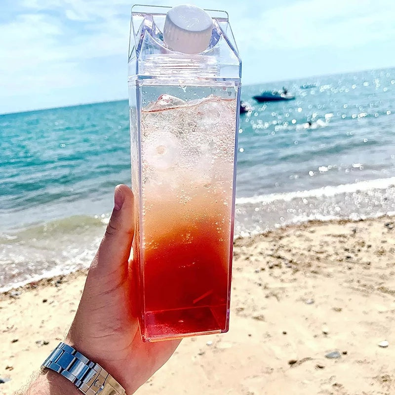 Hand holding a clear container with a red liquid on a beach