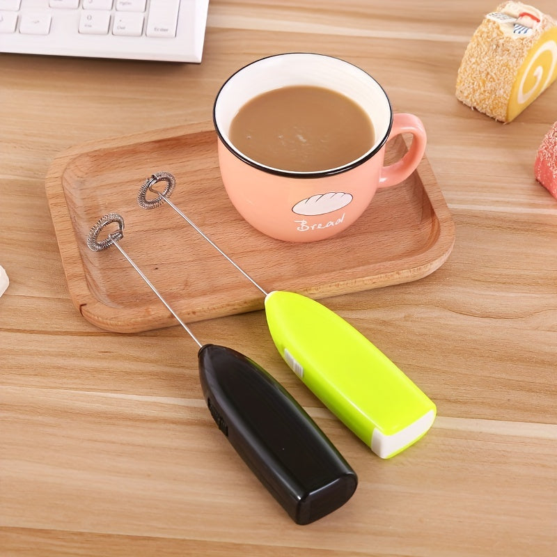Handheld milk frother next to a pink mug with a cloud design on a wooden surface.