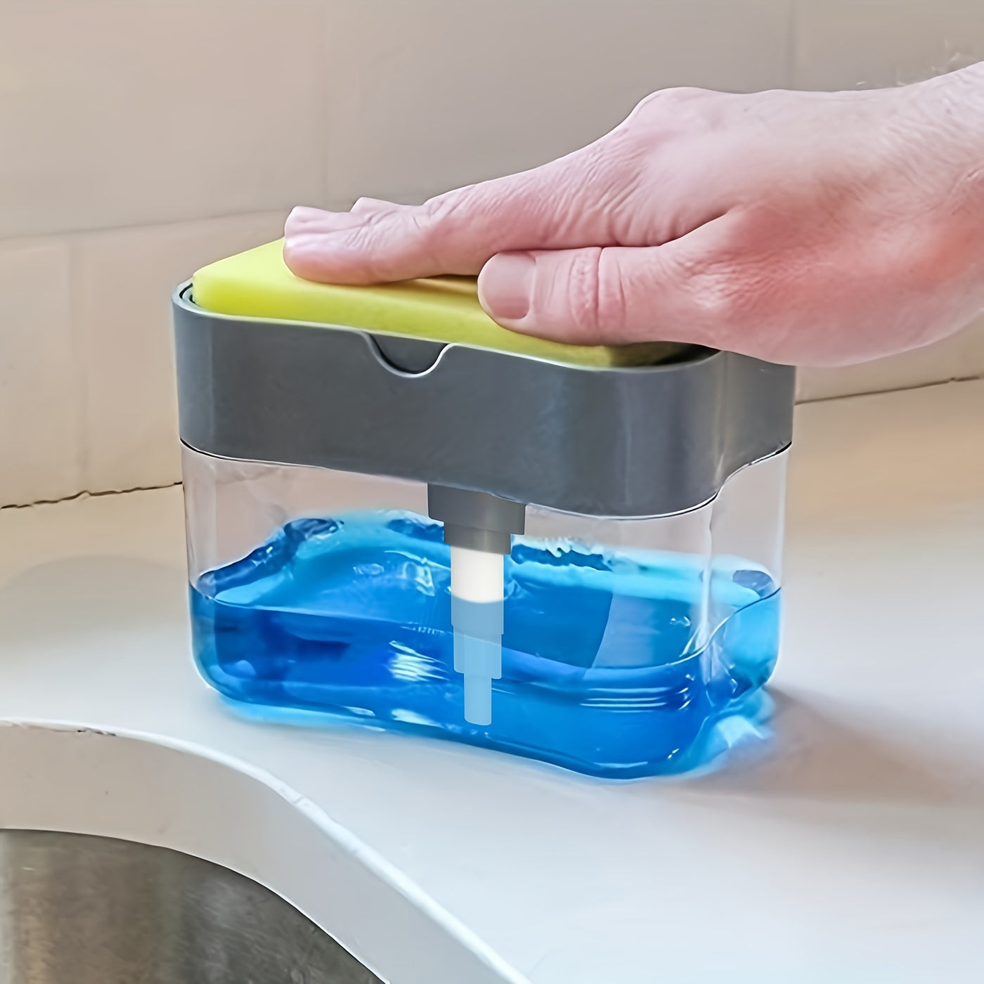 Hand using a blue soap dispenser with a green top on a kitchen counter.