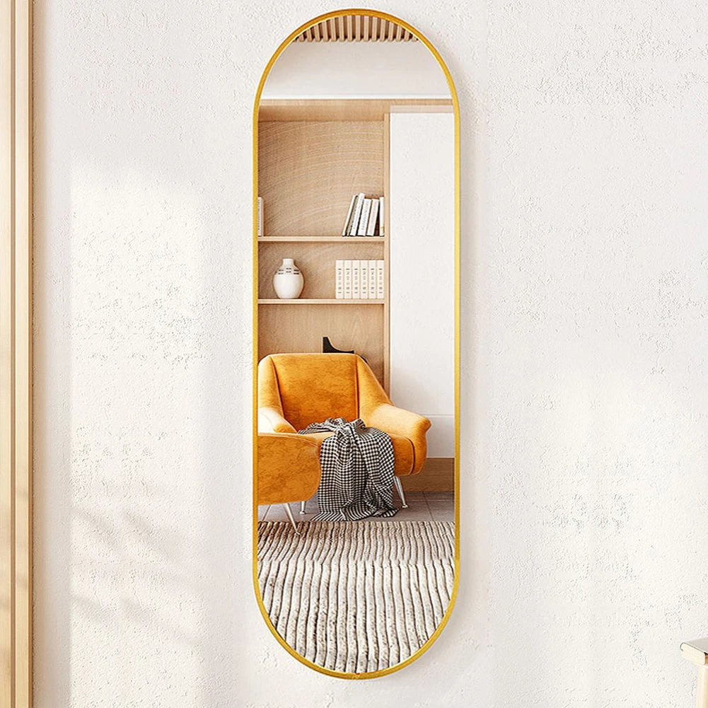 Full-length mirror with gold frame reflecting a room with a yellow armchair and bookshelf.