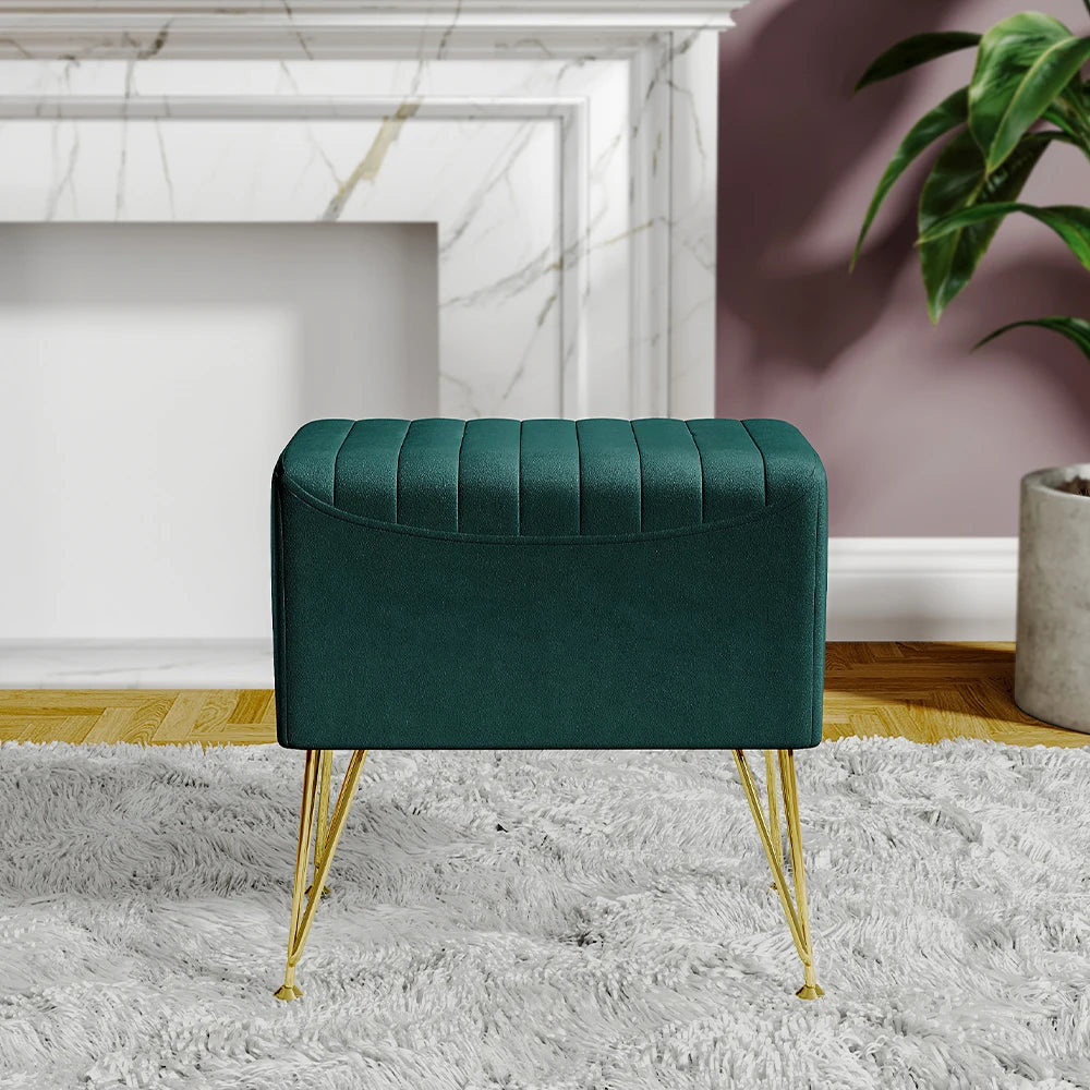 Green ottoman with gold legs in a room with a fireplace and plant