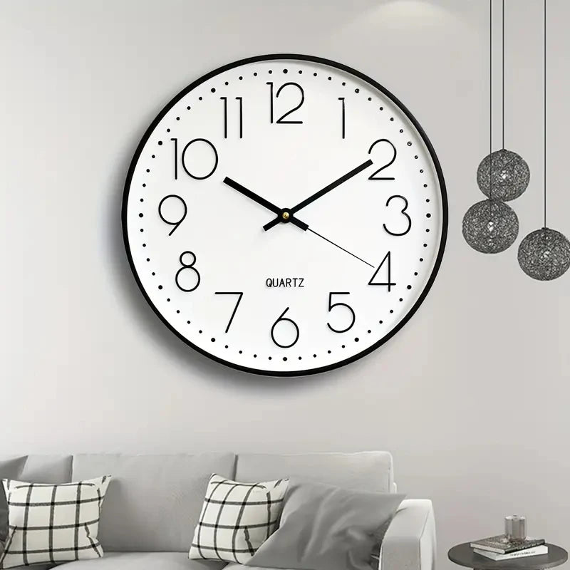 Round wall clock on a white wall above a gray sofa with patterned cushions.