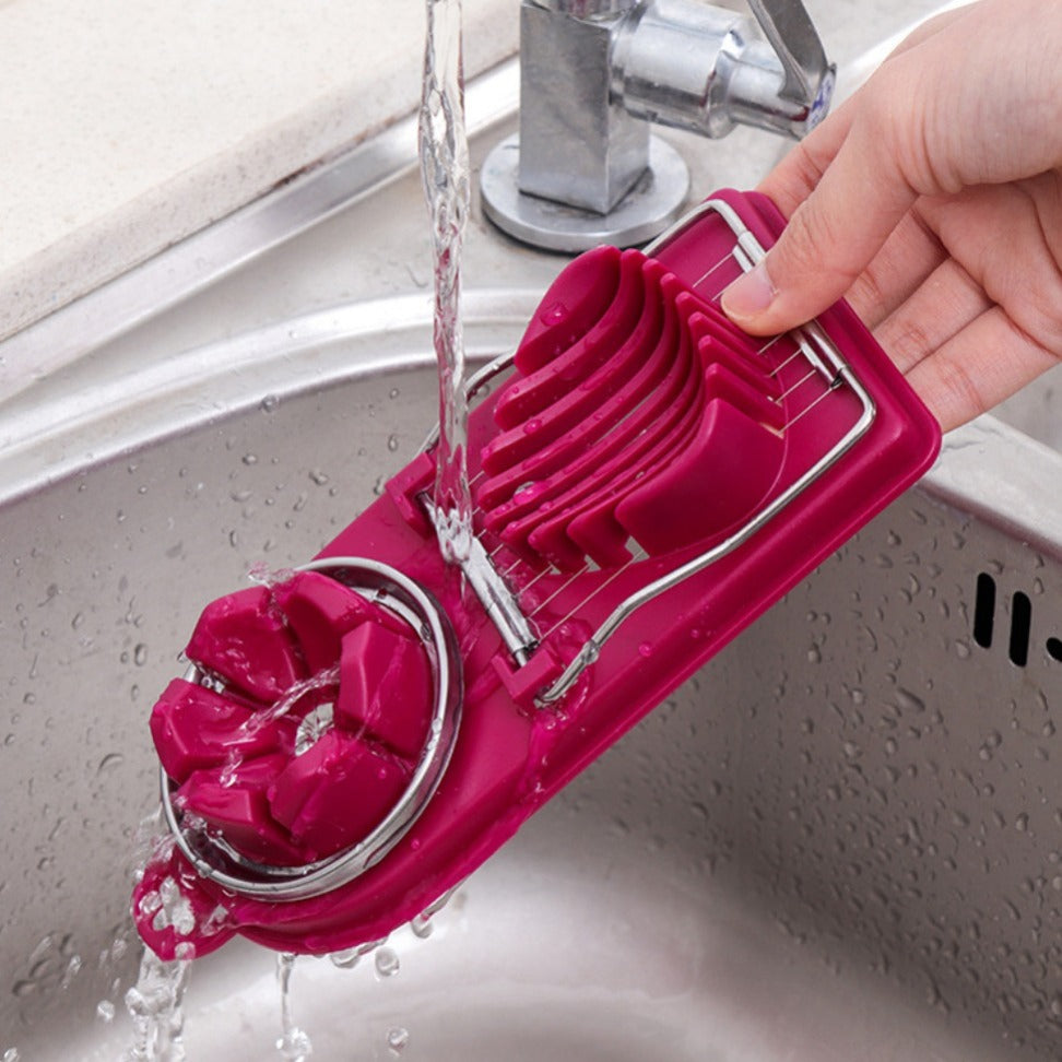 Pink kitchen tool being rinsed under running water in a sink