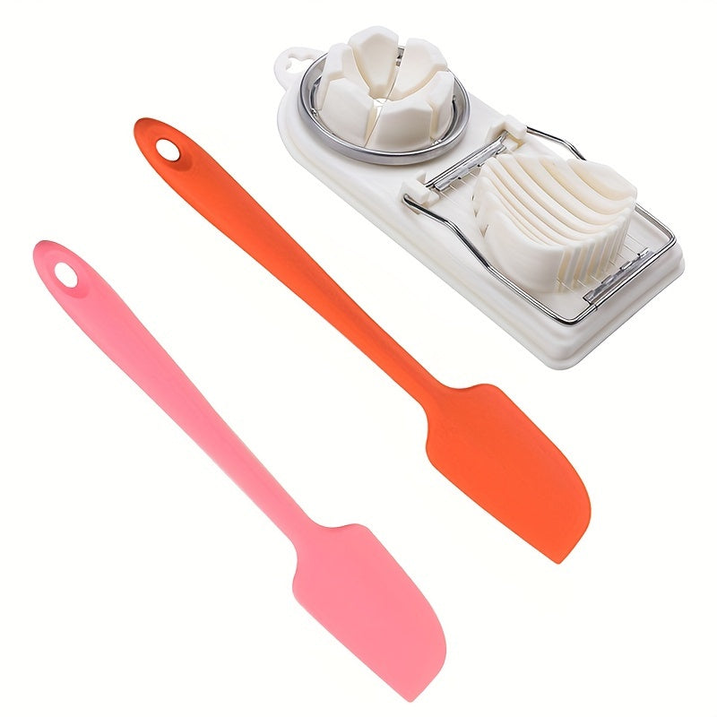 Set of kitchen tools including a white cheese slicer and two silicone spatulas in pink and orange on a white background.