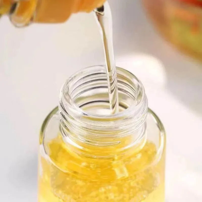 Yellow liquid being poured into a clear glass bottle with a blurred background