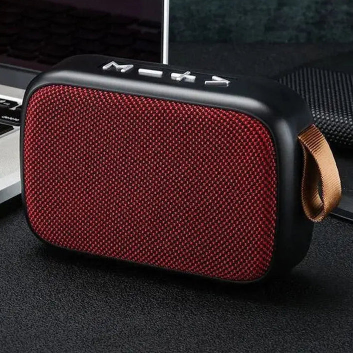 Red portable speaker with black accents on a dark surface next to a laptop.