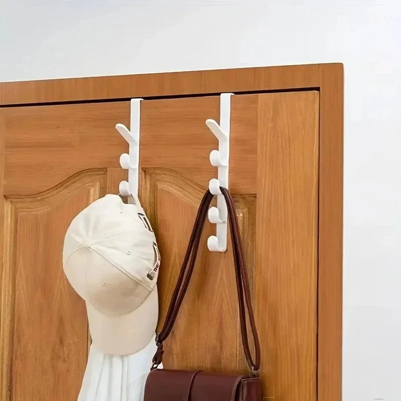 White wall hooks on a wooden door with a cap and bag hanging from them.