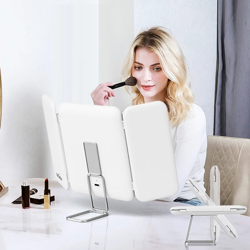 Woman applying makeup with a brush in front of a white mirror on a table.