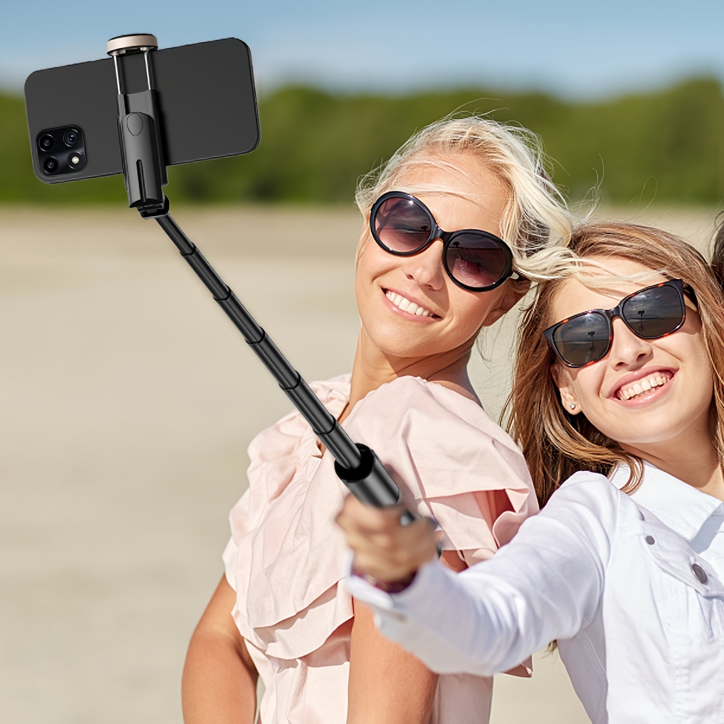 Two women taking a selfie with a smartphone holder on a beach.